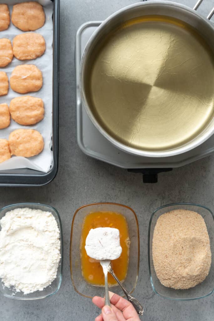 Coating a homemade chicken nugget in flour before dipping it into egg.