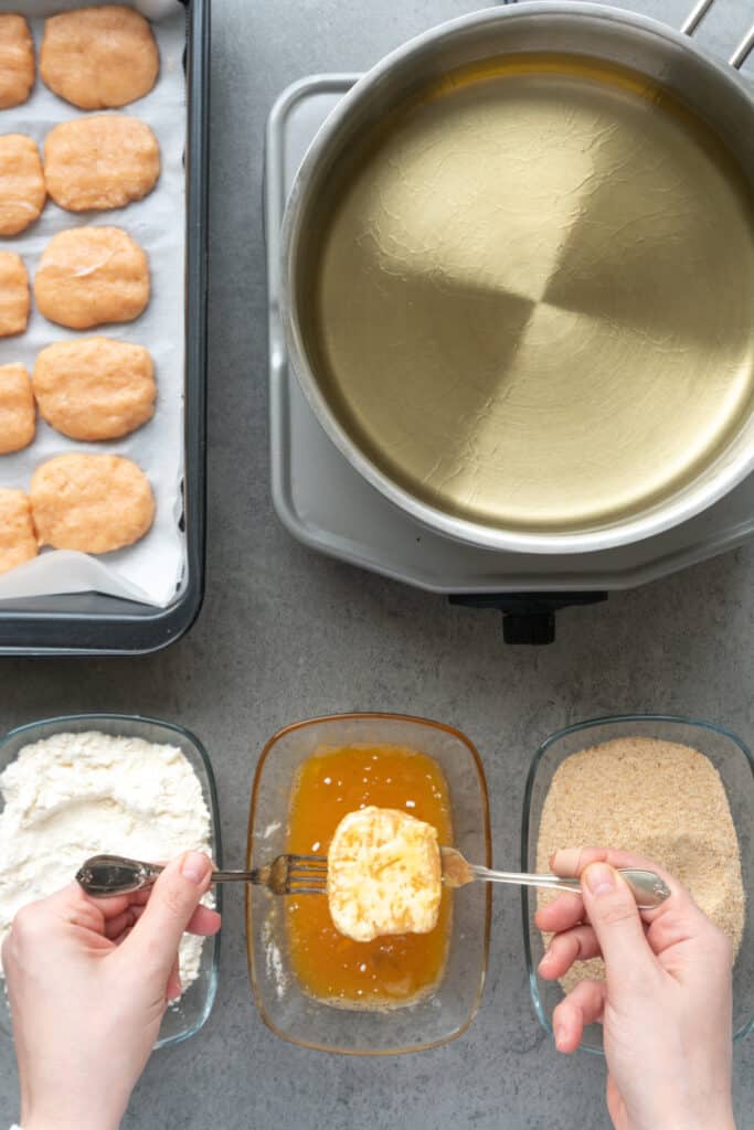 Dipping a floured homemade chicken nugget into beaten egg before breading.