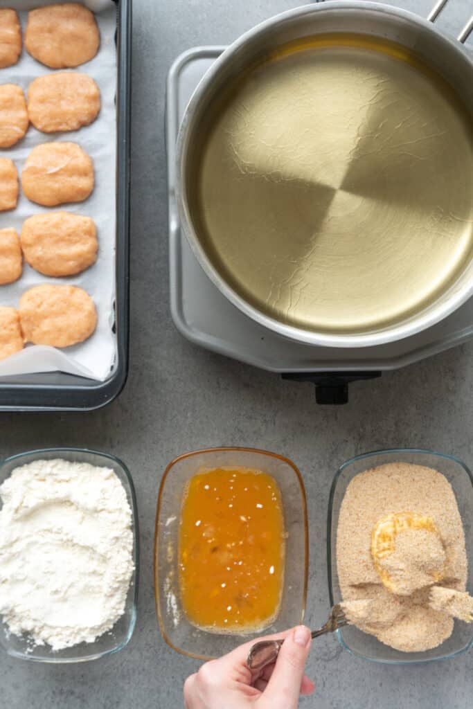 Covering a homemade chicken nugget with seasoned breadcrumbs before frying.
