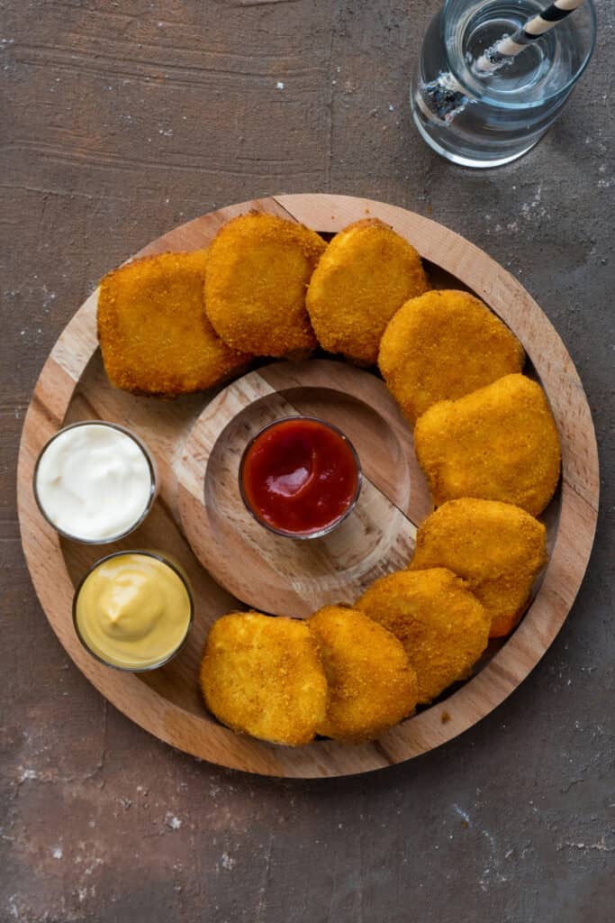 Crispy homemade chicken nuggets served with ketchup, mustard, and mayonnaise for dipping.
