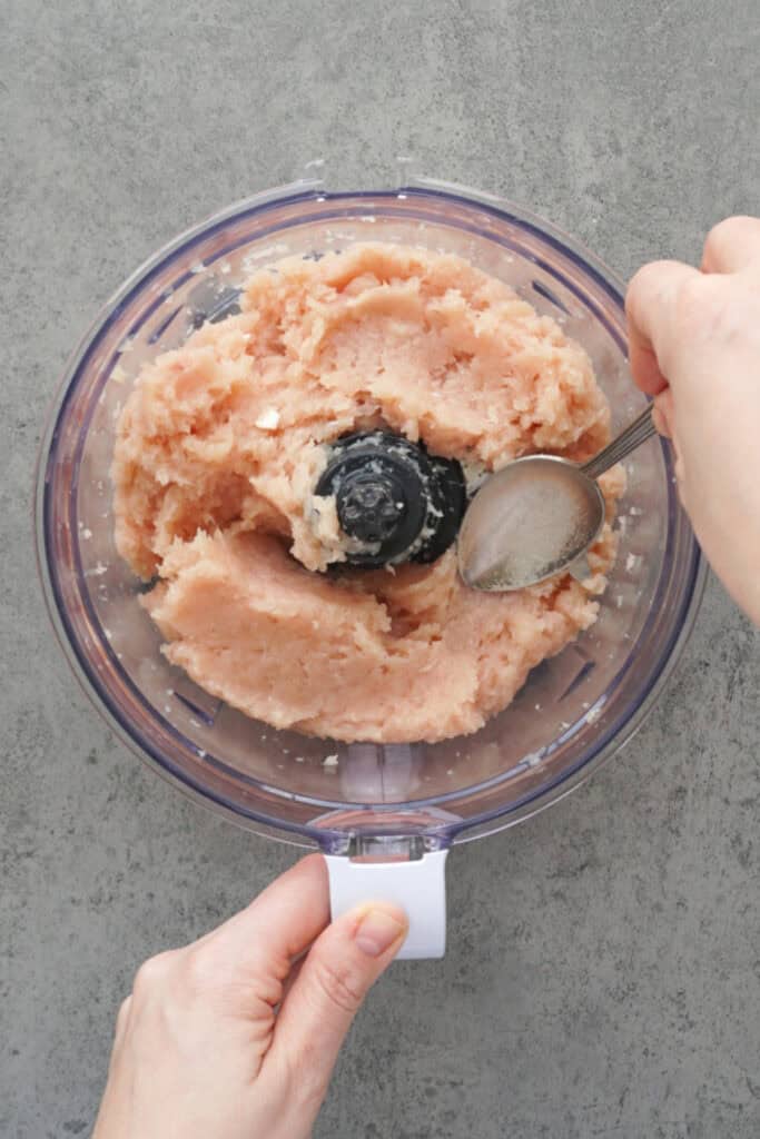 spoon smoothing out chicken in food processor bowl