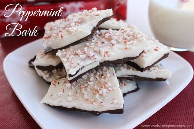Peppermint Bark pieces stacked up on white plate with a glass of milk. Christmas presents in background.