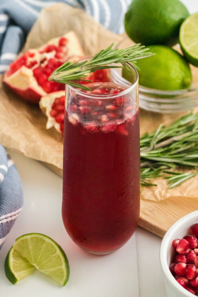 flute filled with pomegranate mimosa and garnished with a sprig of rosemary