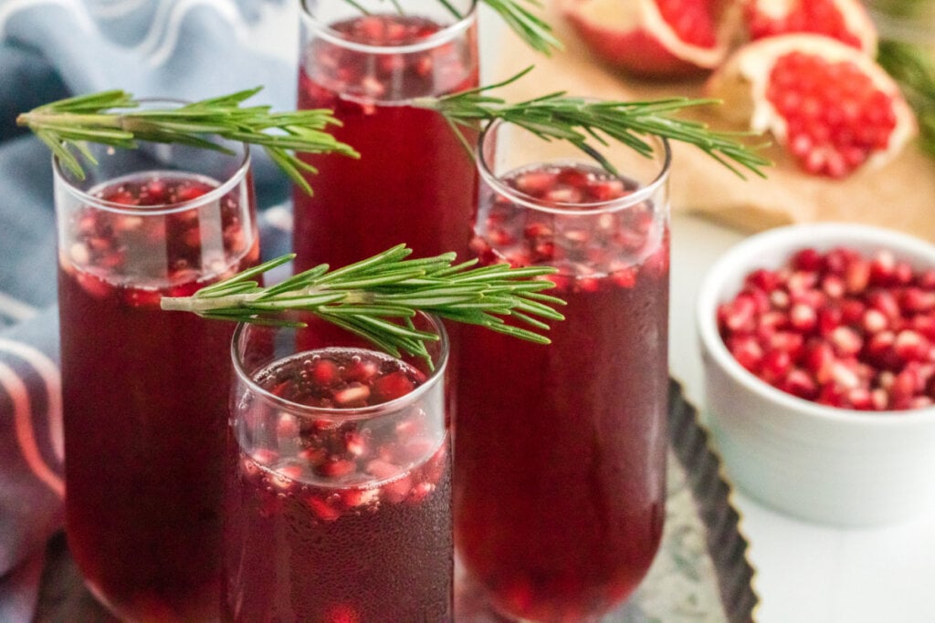 four flutes of pomegranate mimosa on a metal serving platter