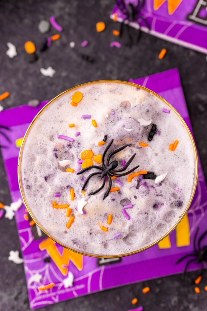 looking down into a glass of purple witch's brew halloween punch with sprinkles and toy spider on top