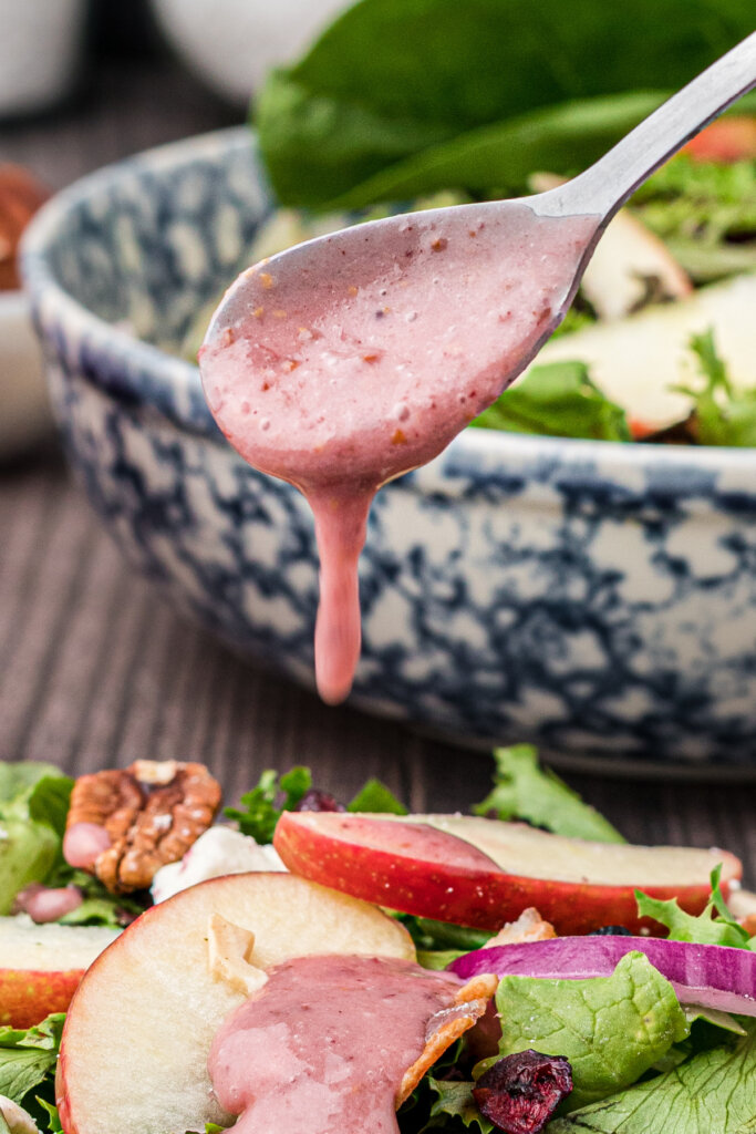 pouring cranberry vinaigrette off spoon onto salad