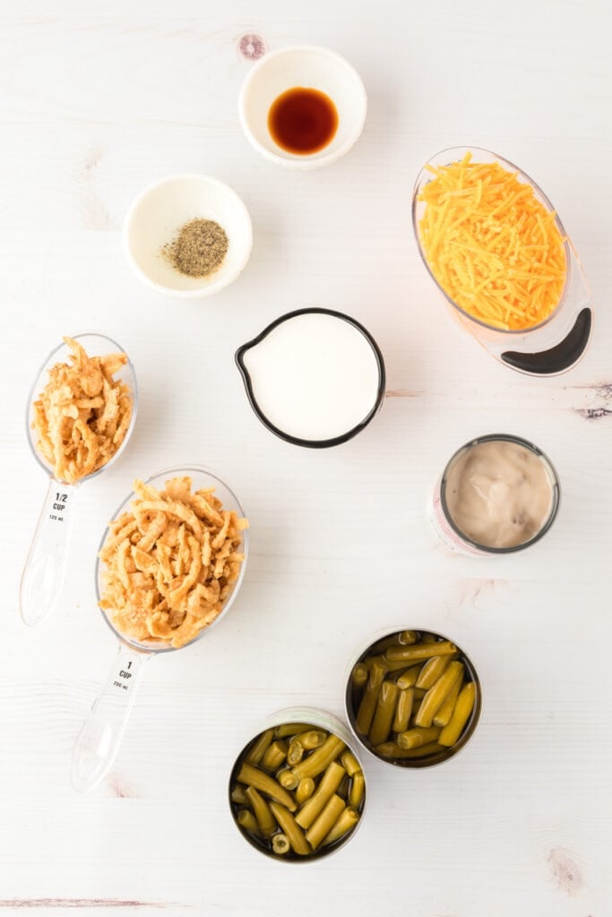 Ingredients for classic green bean casserole including green beans, mushroom soup, cheddar cheese, milk, soy sauce, pepper, and crispy fried onions