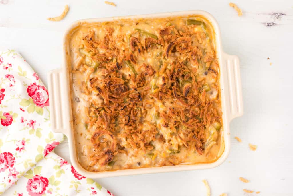 Classic green bean casserole with creamy mushroom sauce and golden crispy fried onions in a square baking dish