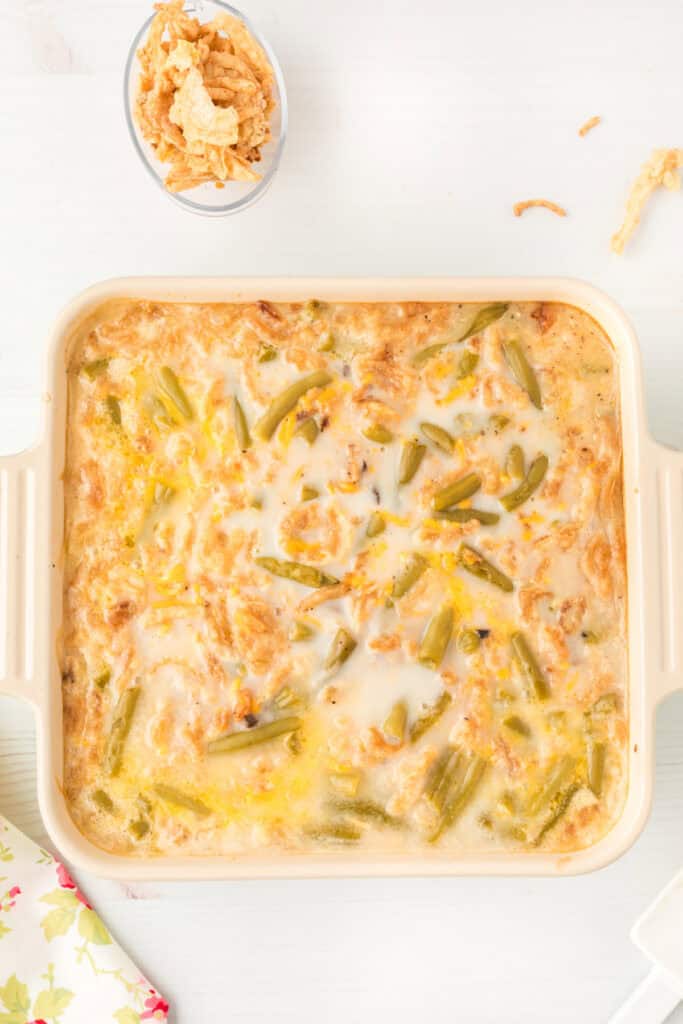Green bean casserole partially baked in a cream-colored casserole dish before adding the final crispy onion topping