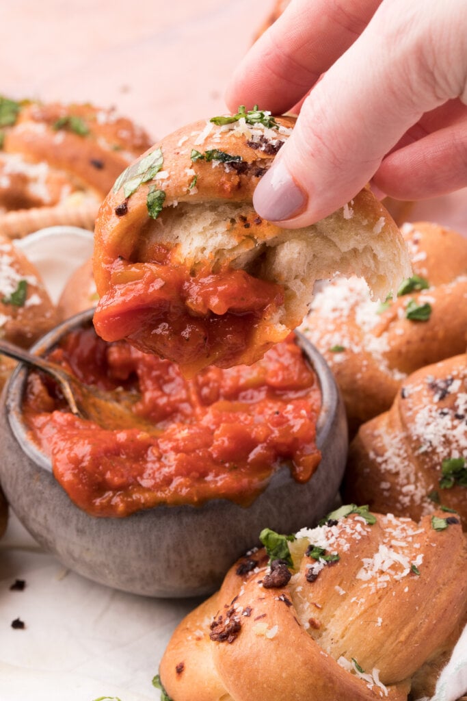 garlic knot being dipped into tomato sauce