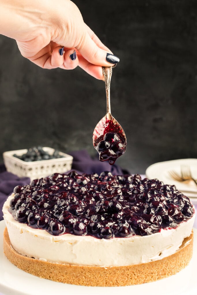 blueberry sauce dropping from spoon onto blueberry cheesecake