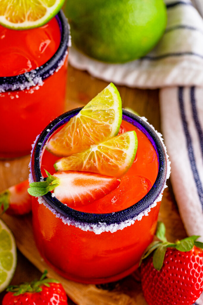 looking down into a strawberry margarita garnished with limes and a strawberry