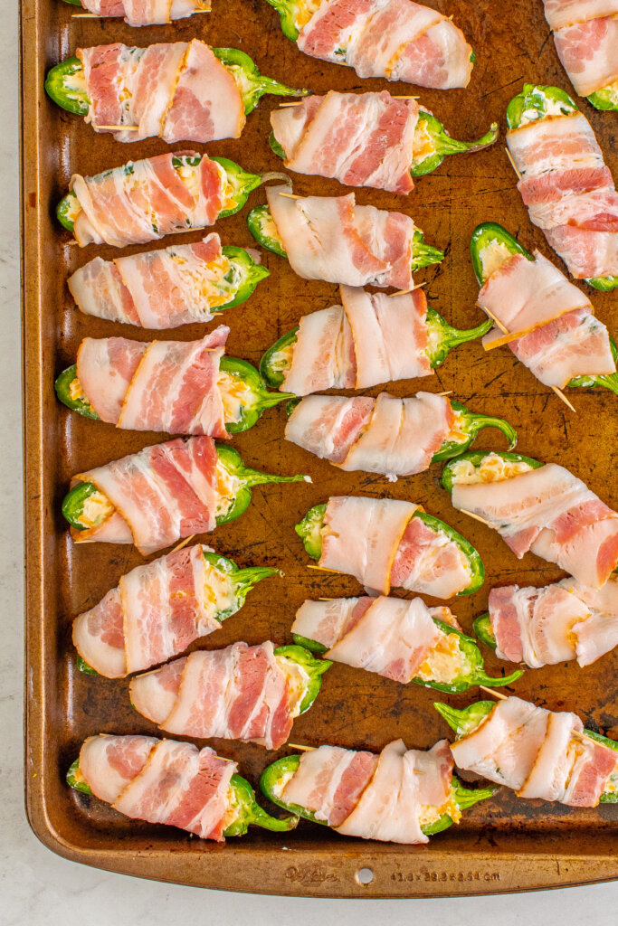 bacon wrapped jalapeno poppers on baking sheet before being cooked