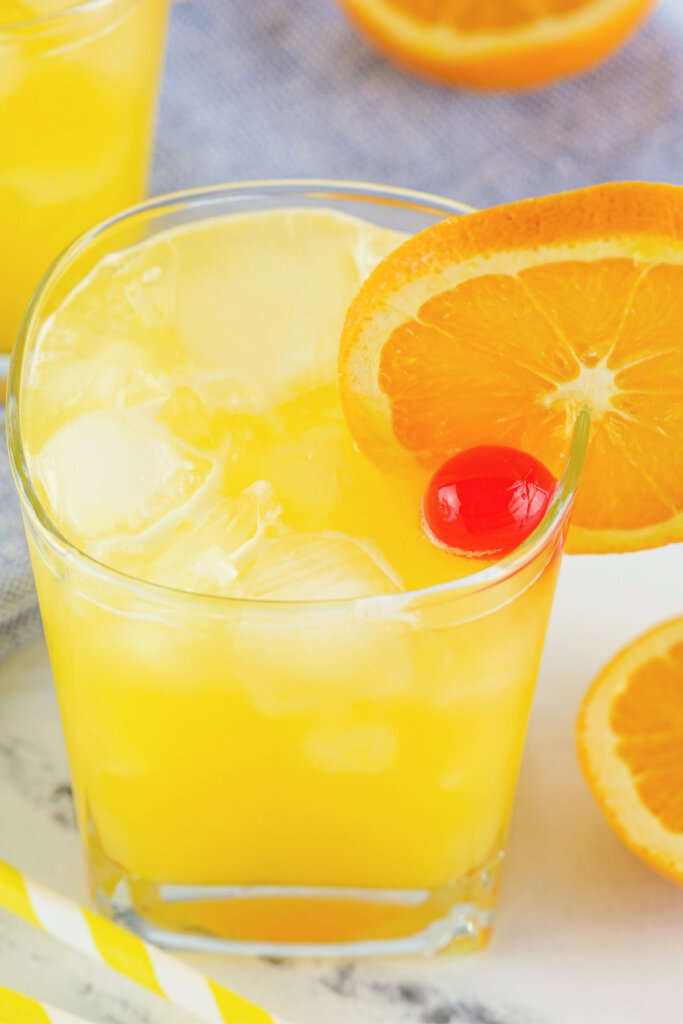 glass with fuzzy navel cocktail garnished with orange wheel and maraschino cherry