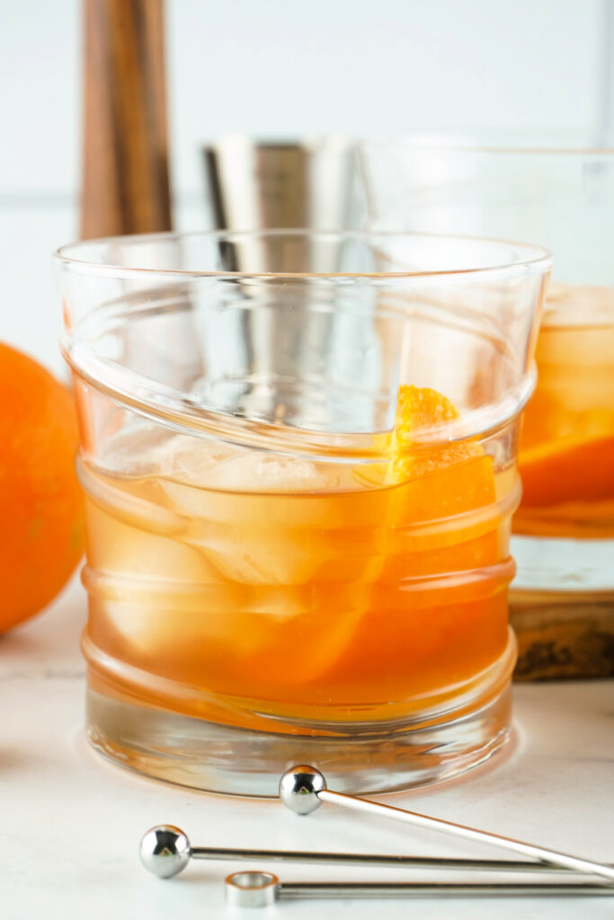 two old fashioned cocktails in glass with stirrers in front