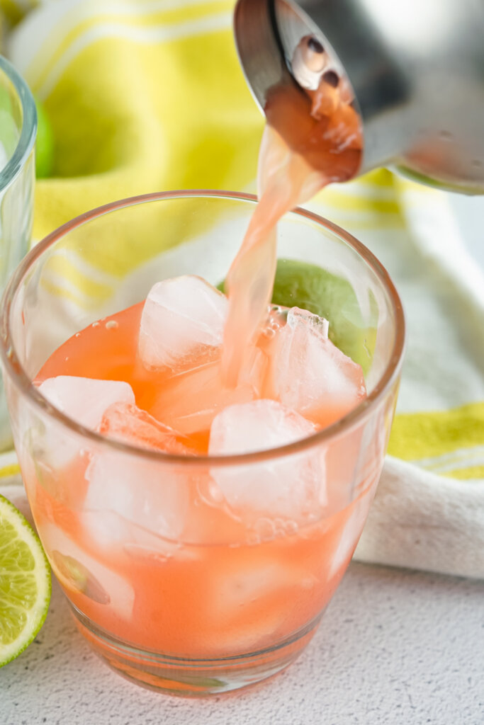 cocktail shaker straining rum punch into serving glass