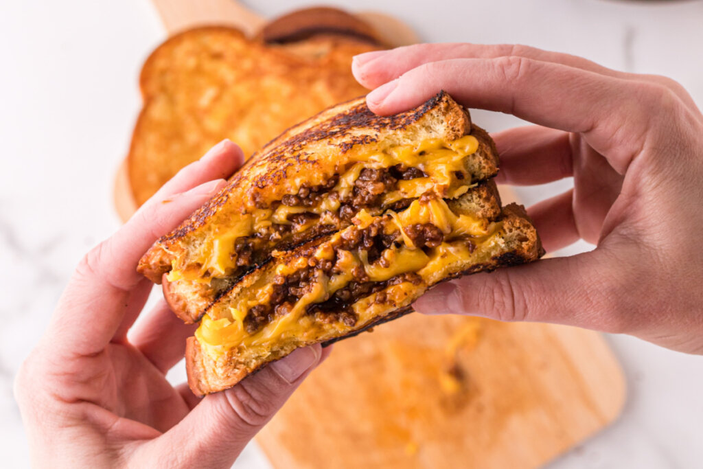 hands holding two halves of a cheesy sloppy joe