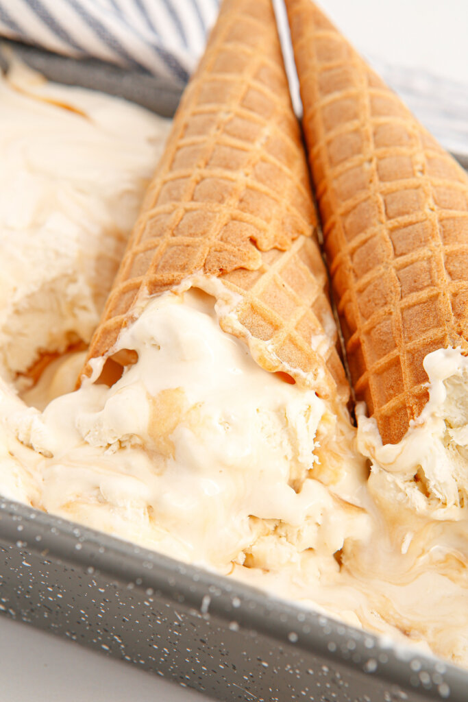 two ice cream cones laying on a container of salted caramel ice cream