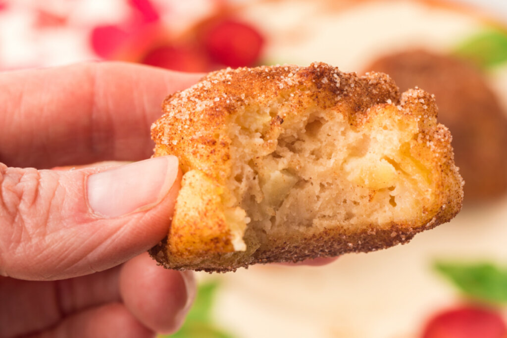 hand holding an apple fritter with a bite taken out