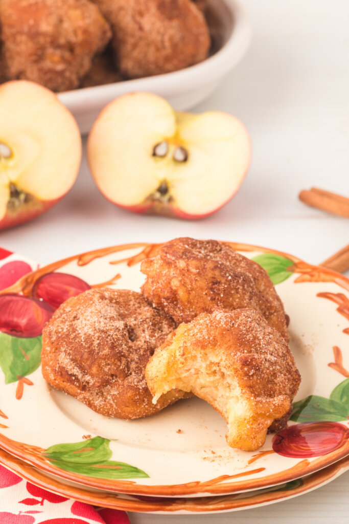 three apple fritters on plate with bite taken out of one