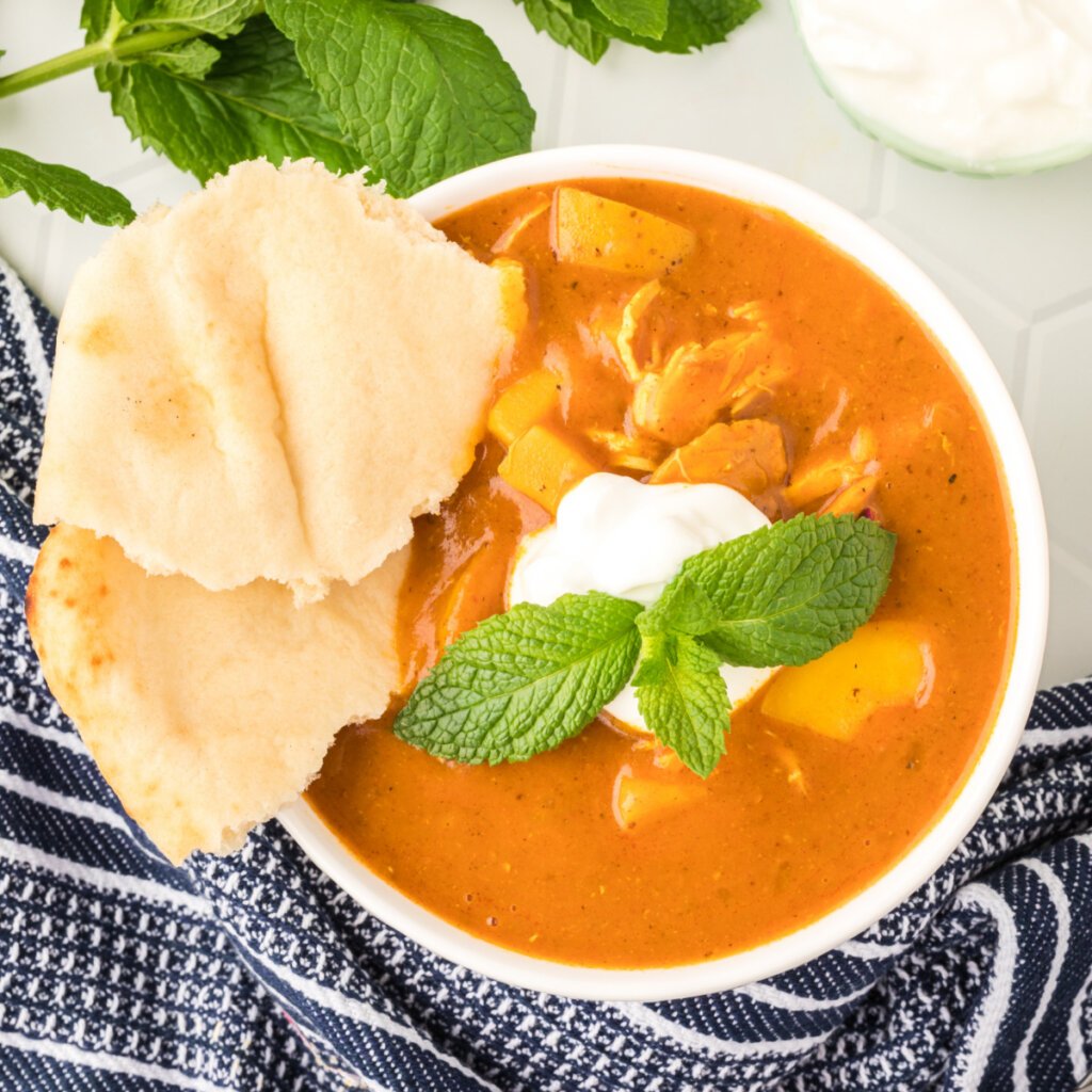 indian spiced chicken potato stew in white bowl garnished with yogurt and mint