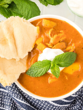 indian spiced chicken potato stew in white bowl garnished with yogurt and mint