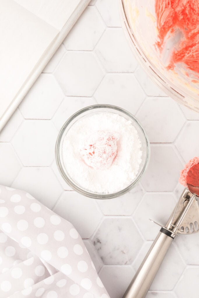 A pink cookie dough ball fully coated in powdered sugar