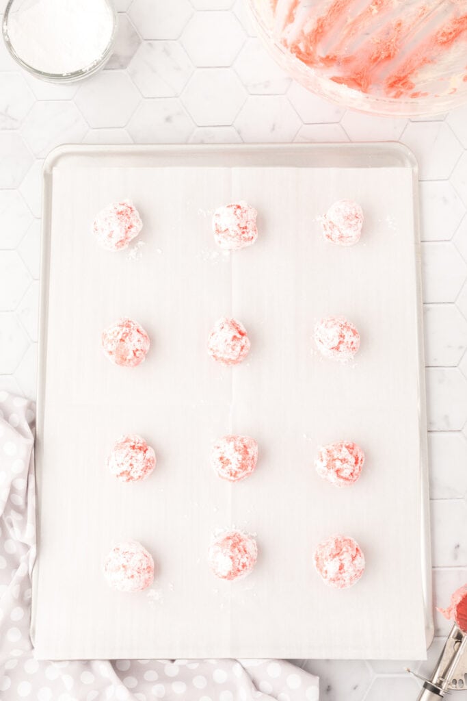 Powdered sugar coated pink dough balls arranged in rows on a parchment lined baking sheet