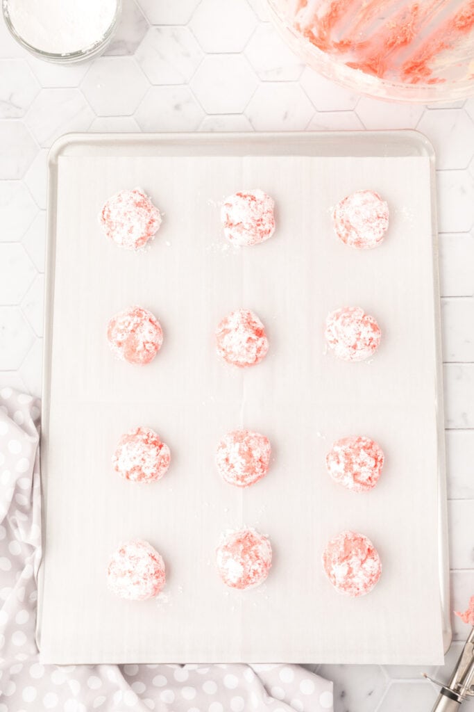 Rounded pink dough balls spaced out on a baking sheet, ready to bake