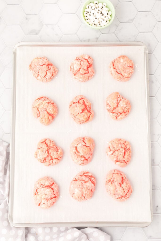 Baked pink crinkle cookies with cracked tops, cooling on a parchment lined baking sheet
