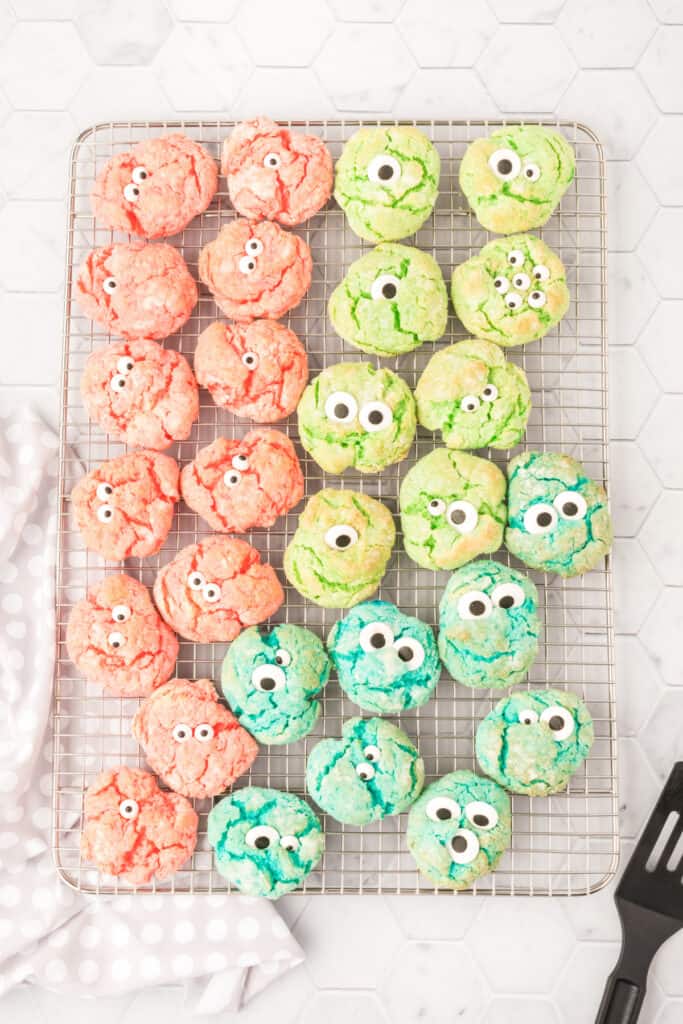 A wire cooling rack filled with pink, green, and blue monster eye cookies decorated with candy eyes