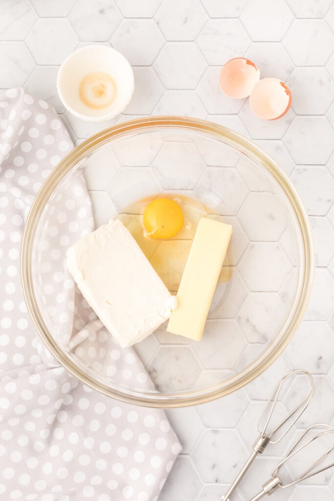 Cream cheese, butter, and an egg yolk in a glass mixing bowl before beating