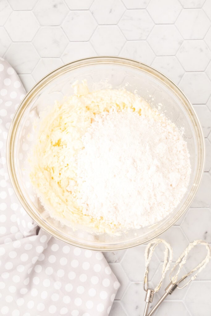 Cake mix added on top of the creamed butter and cream cheese mixture in a glass bowl
