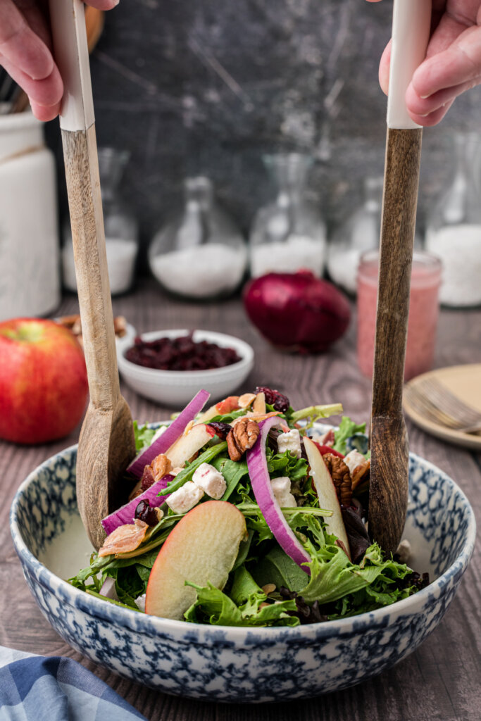 thanksgiving salad being combined with wooden salad tongs