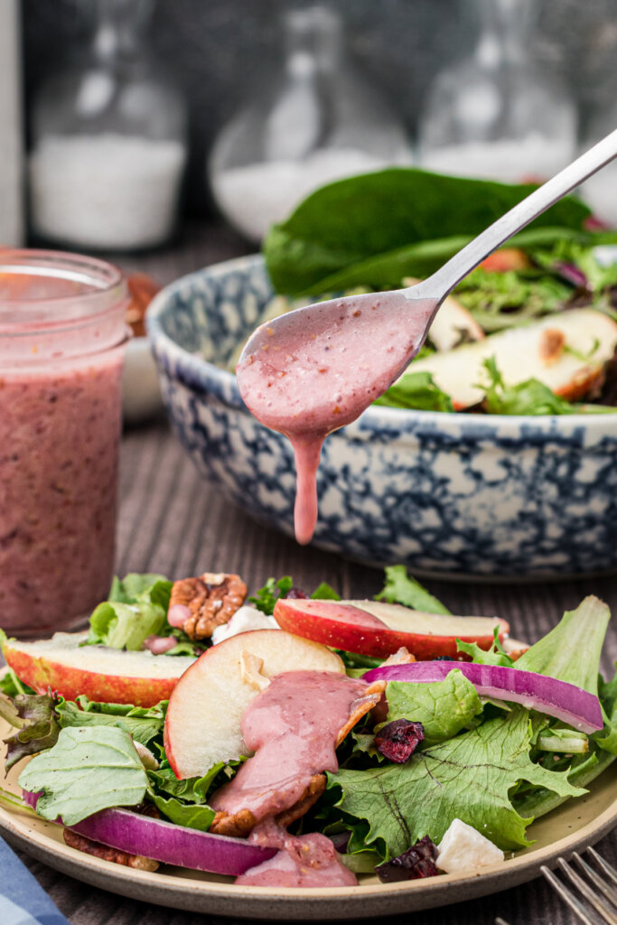 cranberry vinaigrette salad dressing being poured off a spoon onto salad