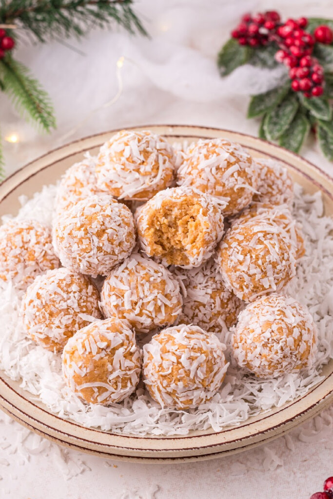 coconut snowballs stacked on plate with bite taken out of one of them