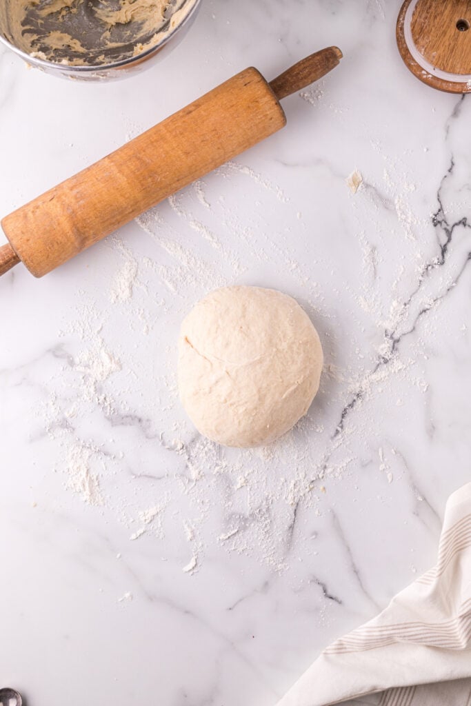 Ball of Texas Roadhouse roll dough on a floured surface beside a rolling pin