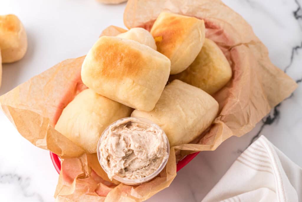 Homemade Texas Roadhouse rolls with cinnamon honey butter in a red basket