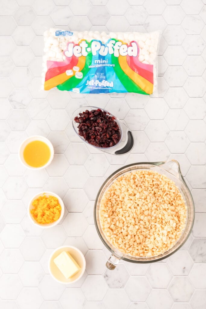 Ingredients for Cranberry Orange Rice Crispy Treats, including mini marshmallows, dried cranberries, orange juice, orange zest, butter, and crisp rice cereal.
