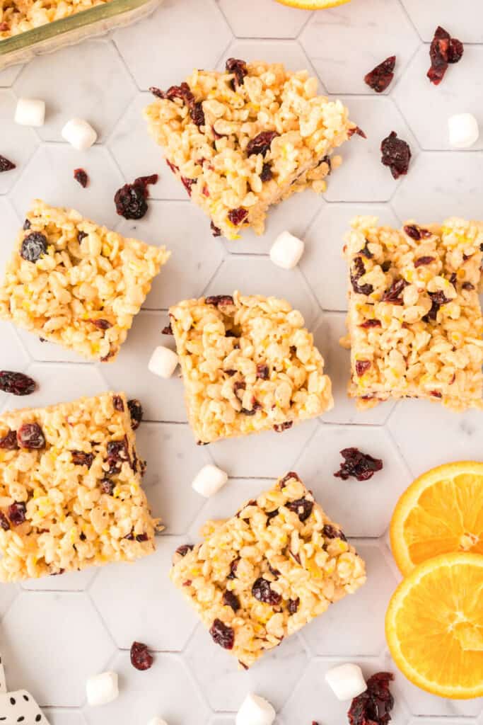 Individual cranberry orange crispy treat squares arranged with dried cranberries, mini marshmallows, and fresh orange slices.