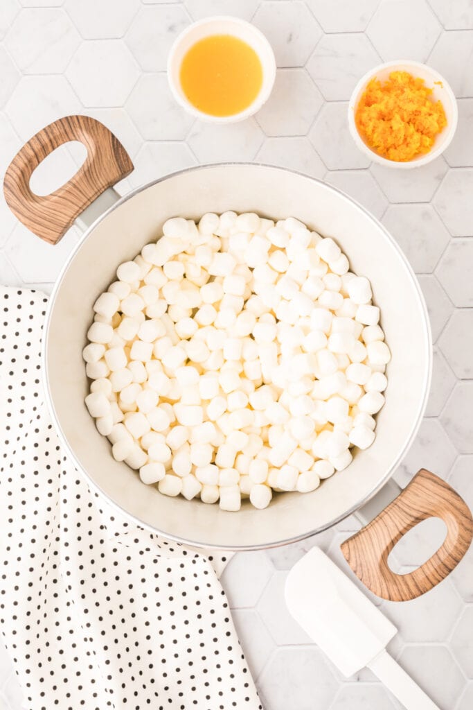 Mini marshmallows beginning to melt in a saucepan for cranberry orange rice crispy treats.
