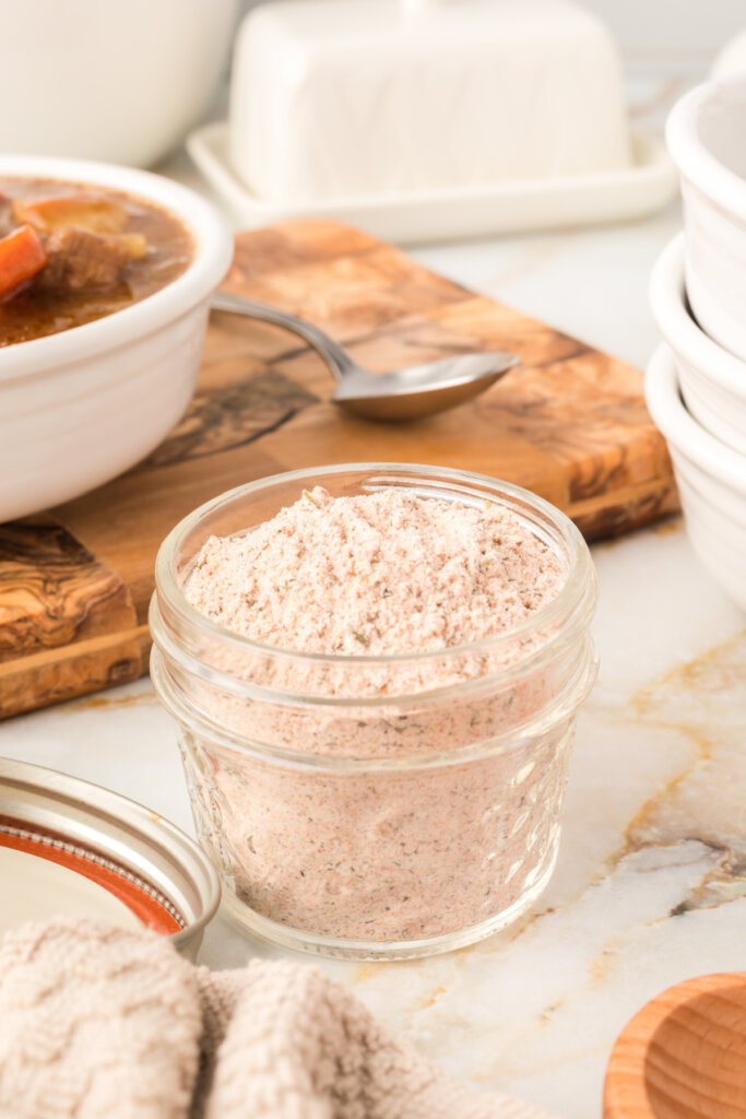 glass jar filled with beef stew seasoning mix with a bowl of beef stew peeking in the background