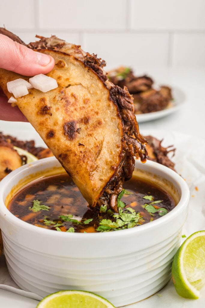 hand dipping a birria taco into consommé