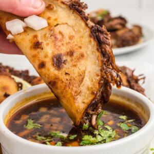 hand dipping birria taco into consommé