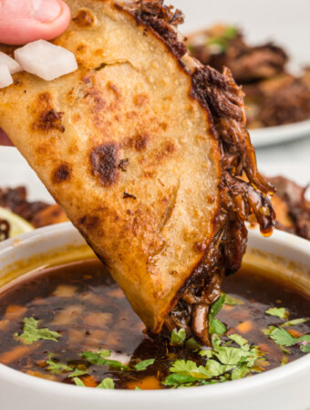 hand dipping birria taco into consommé