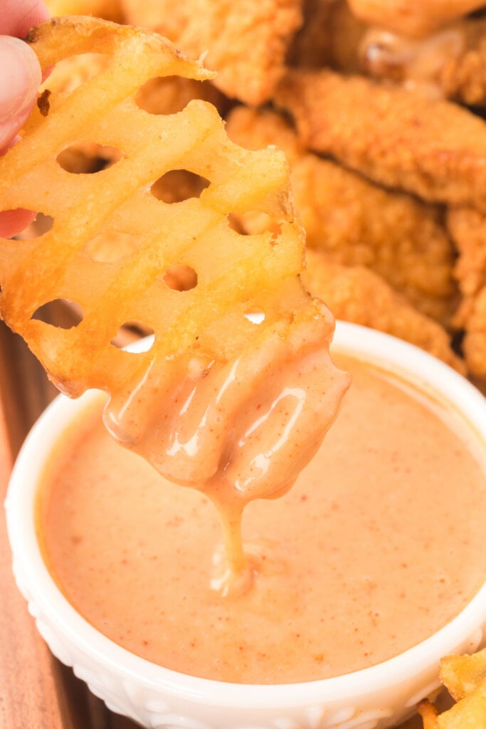 closeup of a waffle fry being dipped into honey roasted bbq sauce