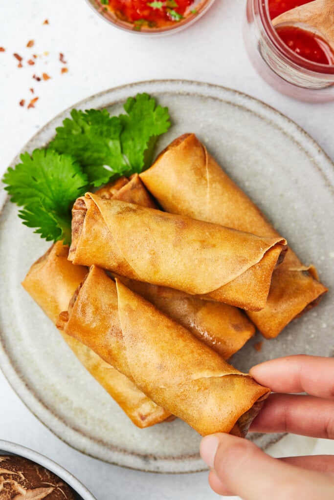 hand reaching in to take spring roll off plate