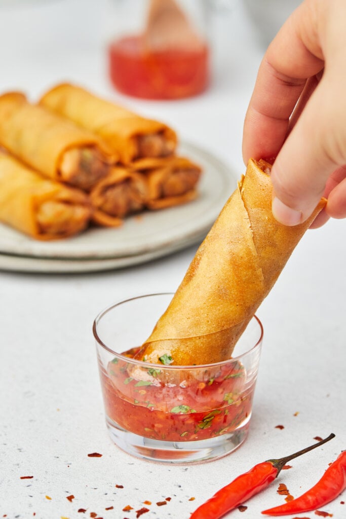 hand dipping spring roll into sweet chili sauce