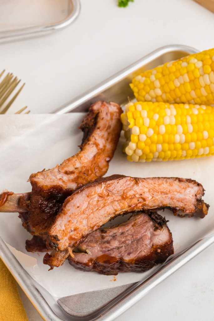 pieces of oven baked ribs on serving tray with corn on the cob
