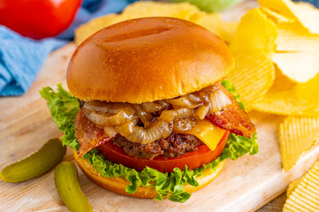 bacon cheeseburger on wooden cutting board with potato chips